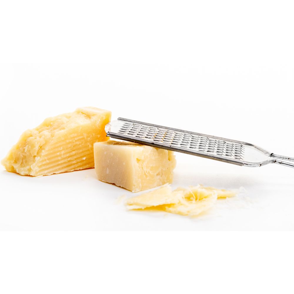 A stainless steel grater with shredded cheese resting on a clean white surface.