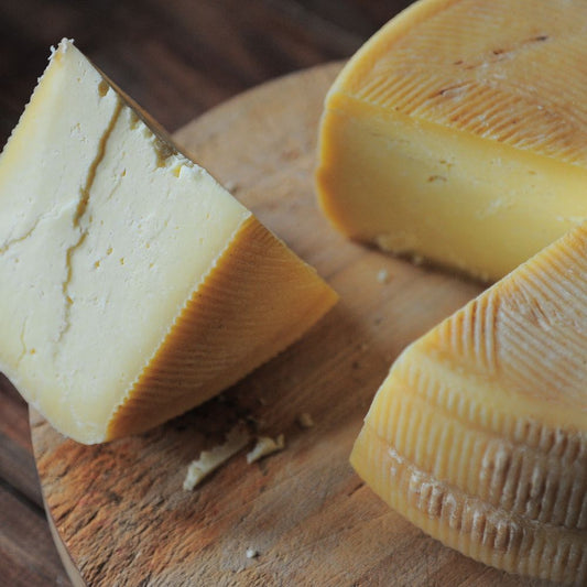 Close-up of a round cheese wheel resting on a rustic wooden board, showcasing its texture and color.