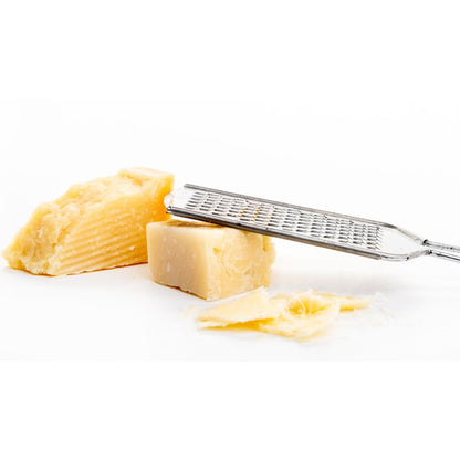 A stainless steel grater with shredded cheese resting on a clean white surface.