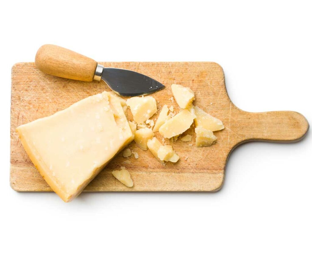 A piece of cheese sits on a wooden cutting board next to a knife, ready for slicing or serving.